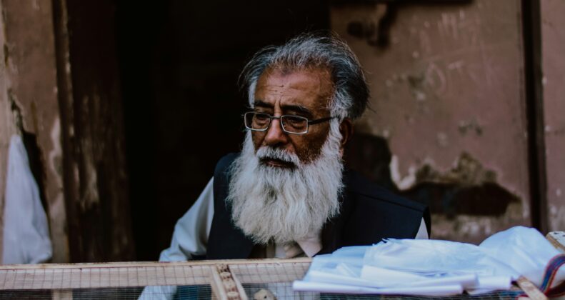 a man with a white beard and glasses sitting in a cage with chickens